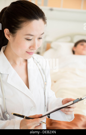 Ritratto di sorridere medico tenendo un grafico medico con il paziente sdraiato in un letto di ospedale in background Foto Stock