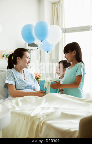 Ragazzo e una ragazza visitando la loro madre in ospedale, dando presente e palloncini Foto Stock