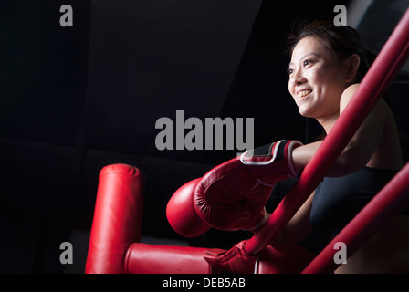 Sorridente boxer femmina in appoggio il suo gomito sul lato anello, guardando lontano, a basso angolo di visione Foto Stock