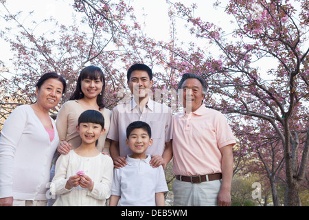 Ritratto di un sorridente multi-generazionale famiglia tra i ciliegi e godere del parco di primavera Foto Stock