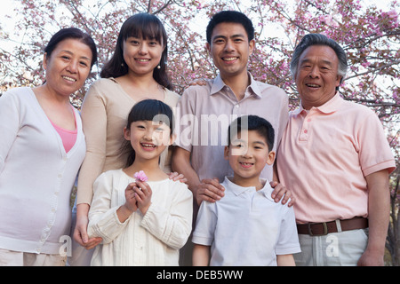 Ritratto di un sorridente multi-generazionale famiglia tra i ciliegi e godere del parco di primavera Foto Stock