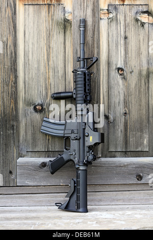 Il fucile nero. 14,5' AR-15 assault carbine (M4A1) con vista olografico contro una vecchia porta di legno. Composizione verticale. Foto Stock