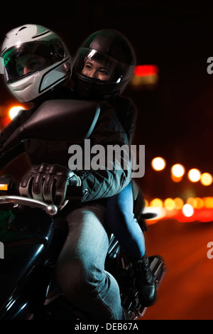 Coppia giovane in sella a una motocicletta per le vie della città di notte a Pechino Foto Stock