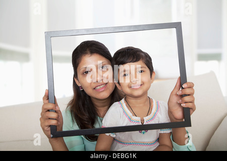 Madre e figlia con in mano una cornice immagine e guardando attraverso di esso Foto Stock