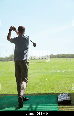 Vista posteriore del giovane uomo colpire palline da golf sul campo da golf, a braccia alzate Foto Stock