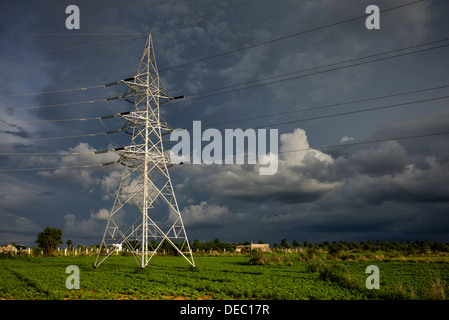 Pilone di elettricità e i cavi nella campagna indiana contro un buio cielo tempestoso. Andhra Pradesh, India Foto Stock