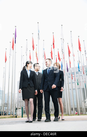 Quattro giovani sorridenti business persone in piedi fuori, bandiere in background Foto Stock