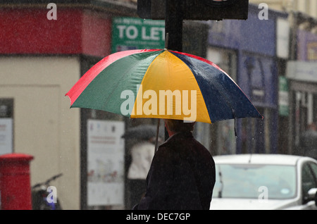 L uomo sta sotto un ombrello coloratissimo sotto la pioggia Foto Stock