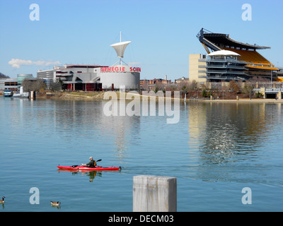 Un canoista pedala lungo il fiume Allegheny a Pittsburgh, vicino alla confluenza con il fiume Monongahela a Point State Park. L'iconico Heinz Field e il Carnegie Science Center sono visibili sullo sfondo. Foto Stock