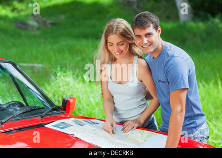 Allegro coppia giovane lettura mappa sulla loro cabriolet cofano Foto Stock