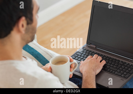 Marrone uomo dai capelli tenendo il caffè usando il suo computer portatile Foto Stock