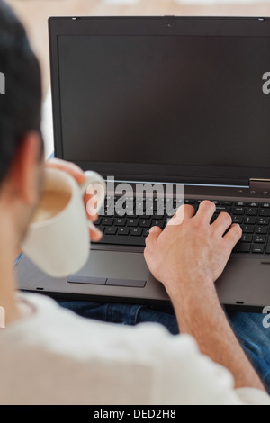 Sulla spalla vista del giovane uomo usando il suo computer portatile Foto Stock