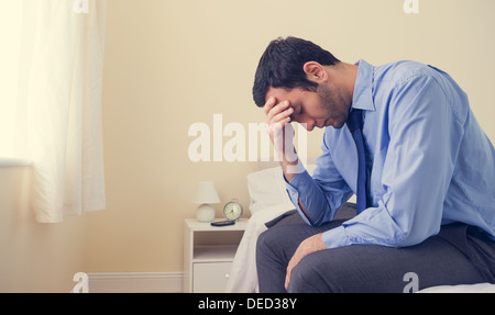 Premuto uomo seduto in testa le mani sul suo letto Foto Stock