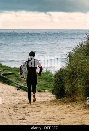 Surfer corre verso l'oceano a Constantine Bay Cornwall Foto Stock