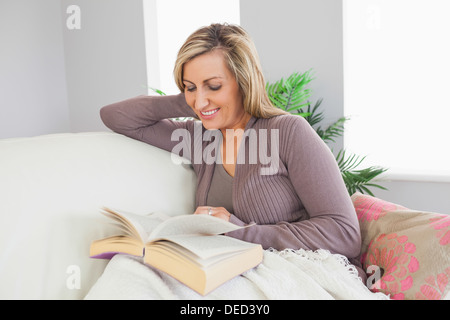Donna sorridente la lettura di un libro su un divano Foto Stock