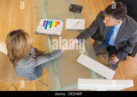 Due persone di affari avente una stretta di mano sopra una scrivania Foto Stock