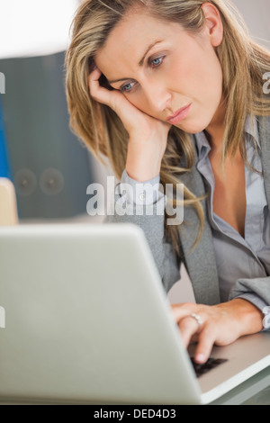 Jaded imprenditrice guardando il suo laptop in un ufficio Foto Stock