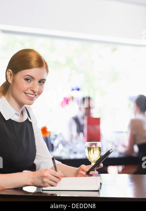 Sorridente imprenditrice iscritto e tenendo il telefono mentre guardando la fotocamera Foto Stock