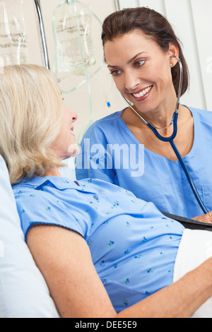 Senior donna femmina paziente in un letto di ospedale essendo curata da una femmina di un infermiere o un medico Foto Stock
