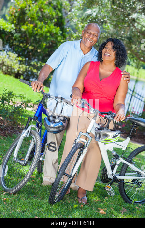Un senior americano africano donna e uomo giovane equitazione biciclette in estate Foto Stock