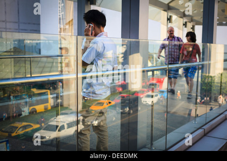 Uomo che utilizza il telefono cellulare sulla strada. Piazza Siam. Bangkok. Thailandia. Foto Stock