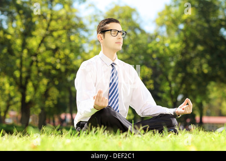 Giovani imprenditori con occhiali meditando seduto su un prato in un parco Foto Stock