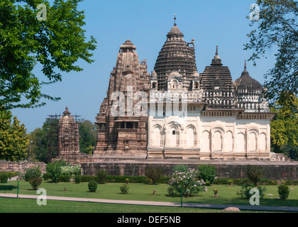 Vecchi e giovani tempio indù, costruito da Chandela Rajputs, presso la Western sito in India di Khajuraho incorniciata dagli alberi. Foto Stock