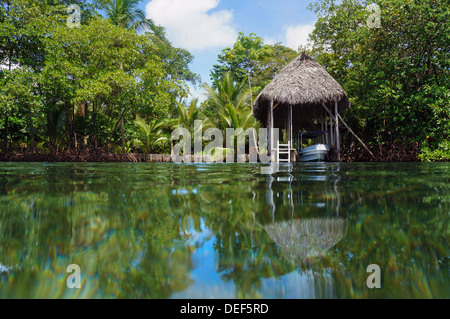 Il Boathouse con palm tetto e lussureggiante vegetazione tropicale che si riflette sulla superficie dell'acqua, Bocas del Toro, Mar dei Caraibi, Panama Foto Stock