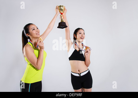 Due giovani donne azienda trofeo indossando medaglie Foto Stock