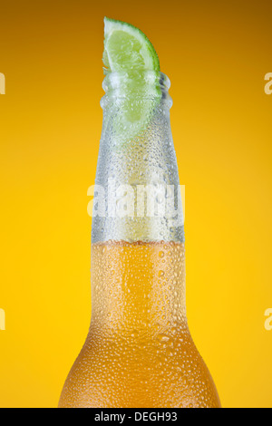 Birra messicana con una fetta di lime su uno sfondo giallo. Foto Stock