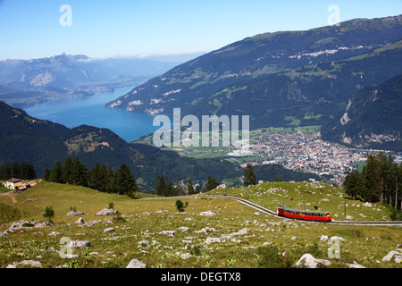 Un rosso treno di montagna con un lago blu in background. Foto Stock