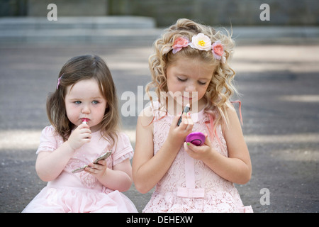 Due ragazze preteen indossando abiti rosa e mettendo il rossetto. Foto Stock