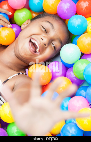 Un giovane americano africano ragazza bambino divertirsi ridere giocare con centinaia di colorate sfere di plastica Foto Stock