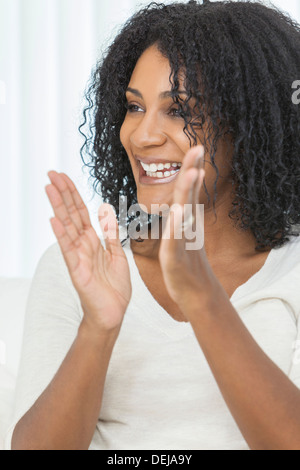 Ritratto di un bellissimo centro di età americano africano donna seduta a casa rilassante ridendo e battendo le mani Foto Stock