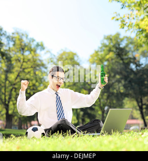 L'uomo il tifo e guardare partite di calcio su un laptop nel parco Foto Stock