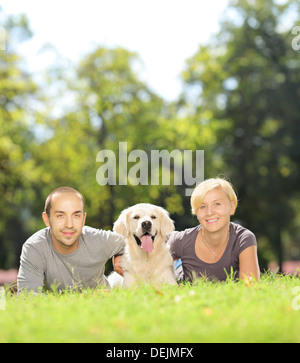 Sorridente coppia giovane sdraiati su un prato verde e abbracciando un cane in un parco Foto Stock