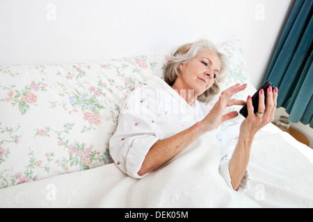 Angolo di alta vista donna senior utilizzando smart phone home letto Foto Stock