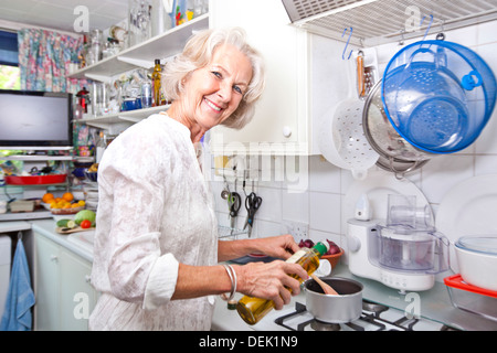 Ritratto di donna senior versando olio d'oliva pentola cucina domestica Foto Stock