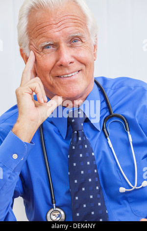 Un sorridenti senior medico maschio seduti ad una scrivania in un ufficio che indossa una camicia e cravatta e uno stetoscopio Foto Stock