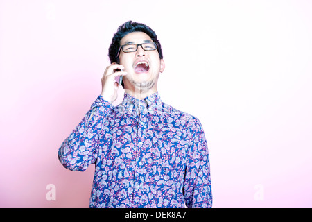 Giovani Geeky Uomo asiatico shirt colorate di ridere sul telefono Foto Stock
