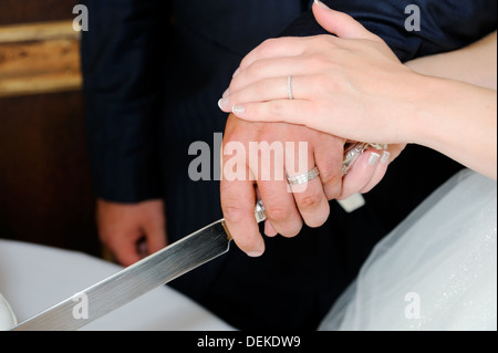 Primo piano della sposa e lo sposo il taglio di torta di nozze presso la reception che mostra gli anelli e coltello Foto Stock