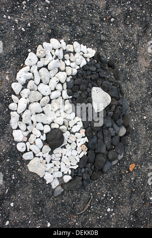 Yin Yang simbolo realizzato da corallo bianco e pietra lavica sulla spiaggia di sabbia nera in Hawaii Foto Stock