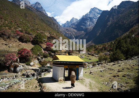 Donna Sherpa trasporta un carico pesante avvicinando una ruota di preghiera gateway sul sentiero da Namche Bazaar verso Thamo e Thame, Nepal Foto Stock