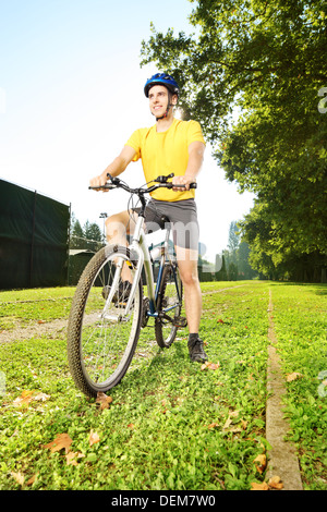 Giovane uomo in maglietta gialla in piedi su una bicicletta in un parco Foto Stock