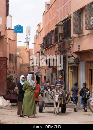 Donne che chiacchierano accanto agli uomini di equitazione in un carro trainato da un asino per le strade di Marrakech, Marocco Foto Stock