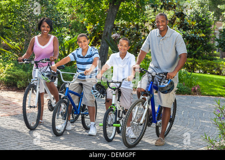 Una giovane famiglia americana africana, donna, uomo, padre, madre e due figli boy bambini equitazione biciclette in estate Foto Stock