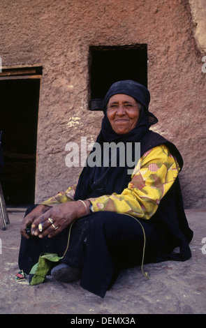 Un'anziana donna beduina dalla tribù Bedul Uno della tribù Huwaitat che storicamente hanno vissuto in Petra indossando abiti tradizionali sorge all'entrata di una caverna residence tagliata nella roccia di Wadi Musa vicino a Petra Giordania Foto Stock