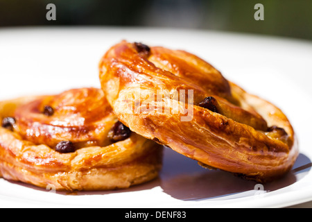 Due acquolina in bocca a scaglie sultana pasticceria danese è su una piastra, all'esterno, su un tavolo al sole Foto Stock