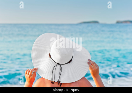 Una donna a prendere il sole su una sedia a sdraio sulla spiaggia e tenendo le mani hat Foto Stock