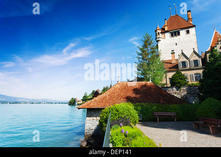 Il lago di Thun e il castello di Oberhofen mura e torri in Svizzera, vista dal parco Foto Stock